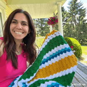 Work-in-progress crochet sports blanket held by designer on sunny patio, customizable in any team colors.